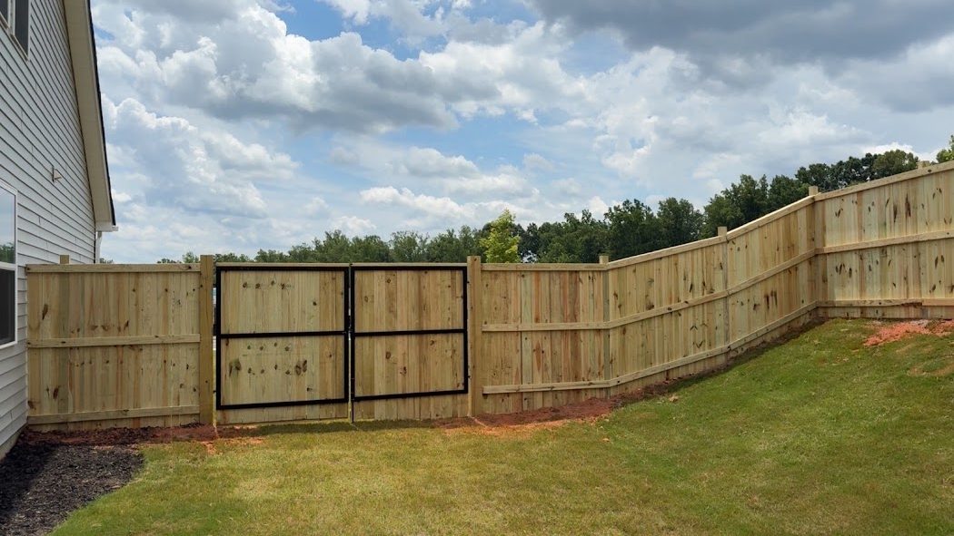 New wood privacy fence with a welded-metal double gate running along a backyard